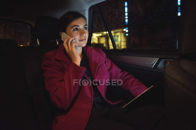 Beautiful businesswoman with digital tablet talking on phone in car — Stock Photo