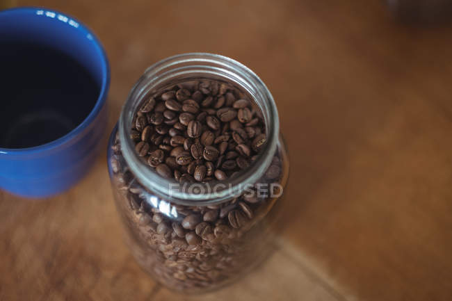 Крупный план банка жареных кофейных зерен и чашки кофе — стоковое фото