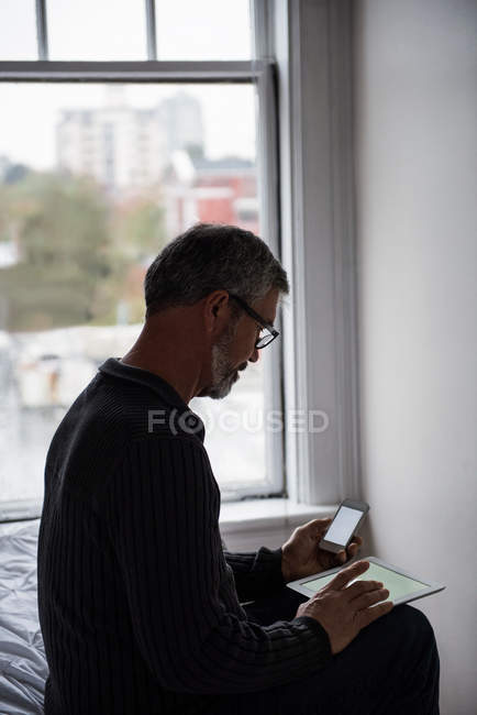 Человек, использующий цифровой планшет и мобильный телефон в гостиной дома — стоковое фото