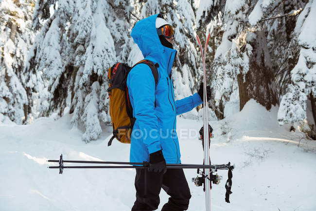 Вид сбоку на лыжника, идущего с лыжами по заснеженным горам — стоковое фото