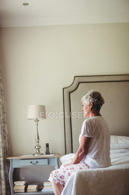 Задумчивая пожилая женщина сидит на кровати в спальне — стоковое фото