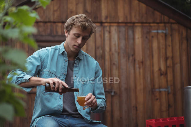 Mann sitzt in Hausbrauerei und schüttet Bier in Bierglas — Stockfoto