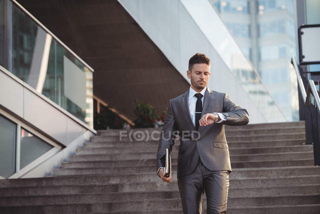 Бизнесмен проверяет время во время спуска по лестнице в офисе — стоковое фото