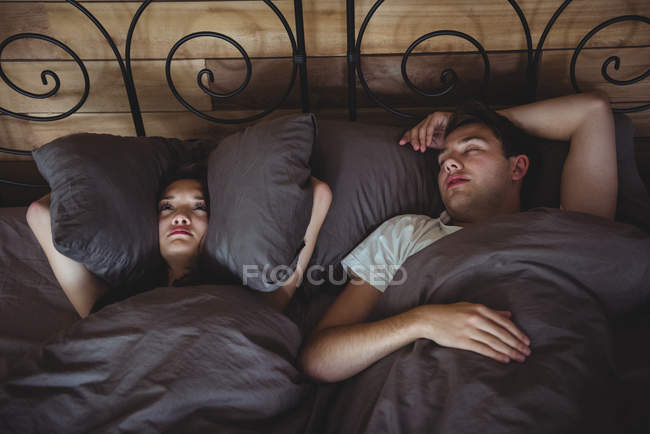Genervte Frau bedeckt ihre Ohren mit Kissen, um das Schnarchen zu Hause im Schlafzimmer zu verhindern — Stockfoto