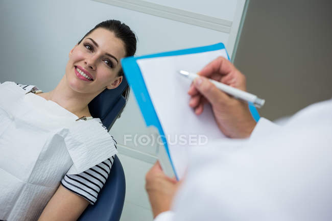 Arzt schreibt auf Klemmbrett, während Patient auf Zahnbett in Zahnklinik liegt — Stockfoto