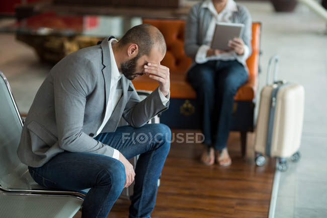 Уставший бизнесмен сидит на стуле в зале ожидания в терминале аэропорта — стоковое фото