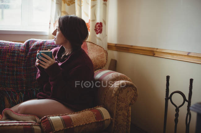 Продумана жінка сидить і тримає чашку кави вдома — стокове фото