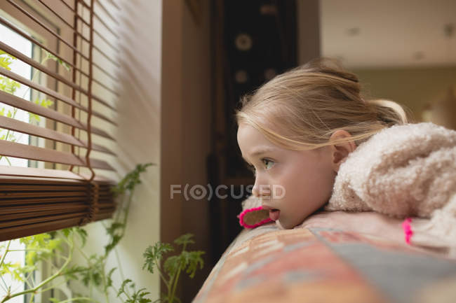 Thoughtful girl looking through window in living room at home — Stock Photo