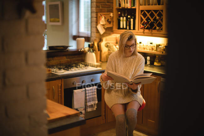 Женщина, читающая книгу дома на кухне — стоковое фото