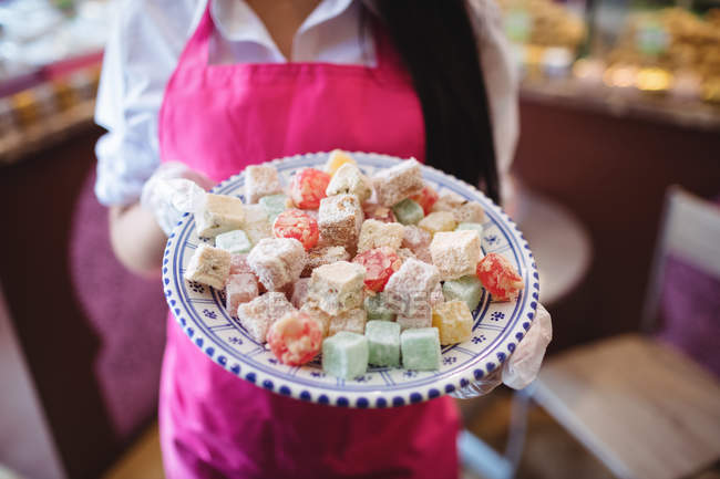 Sección media del tendero femenino sosteniendo bandeja de dulces turcos en el mostrador en la tienda - foto de stock