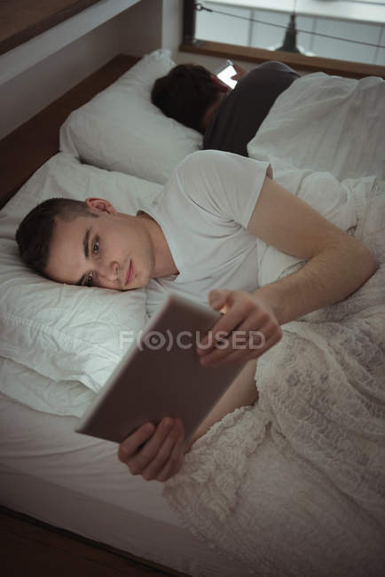 Mann benutzt digitales Tablet, während er mit homosexuellem Partner im Schlafzimmer im Bett liegt — Stockfoto