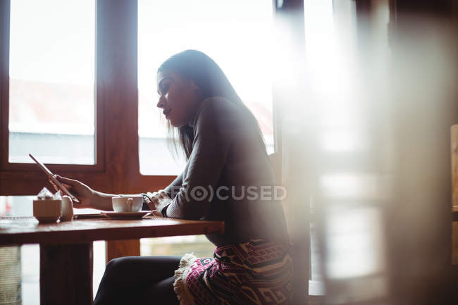 Donna che utilizza tablet digitale mentre prende una tazza di caffè nel caffè — Foto stock