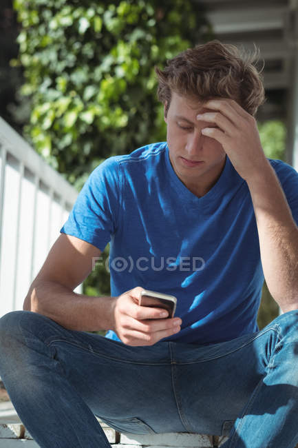 Чоловік сидить на ганку і використовує мобільний телефон — стокове фото