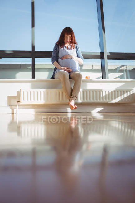 Thoughtful pregnant woman sitting near window in living room at home — Stock Photo