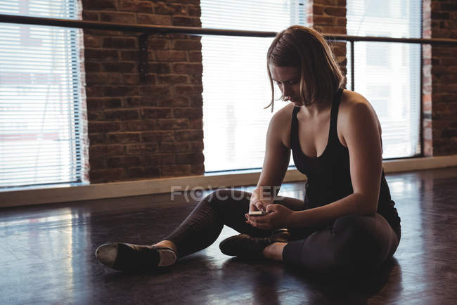 Dancer sitting on floor and using mobile phone in dance studio — Stock Photo