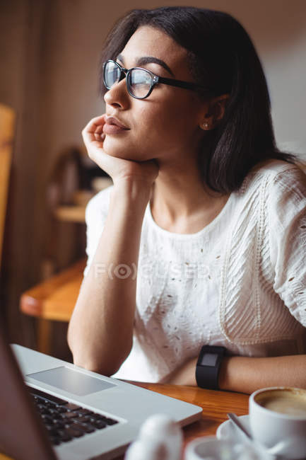 Femme réfléchie assise avec un ordinateur portable dans un café — Photo de stock