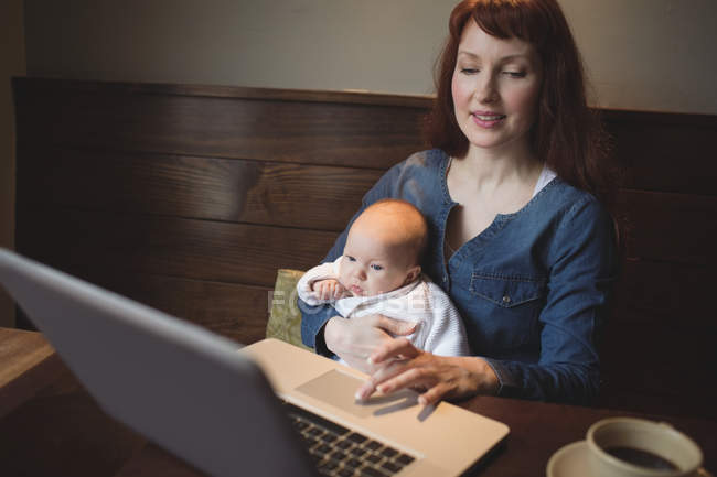 Madre con el bebé usando el ordenador portátil en la cafetería - foto de stock