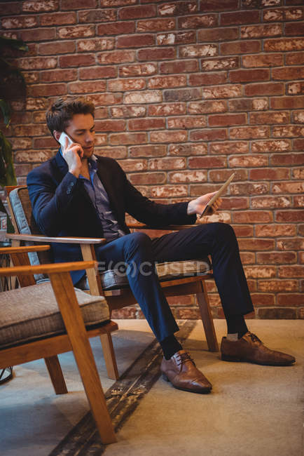 Бізнесмен розмовляє на мобільному телефоні і тримає цифровий планшет в кафе — стокове фото
