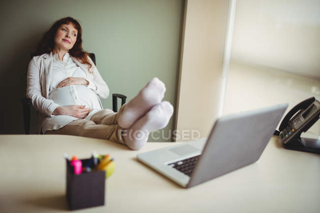 Embarazada mujer de negocios relajarse con los pies en la oficina - foto de stock