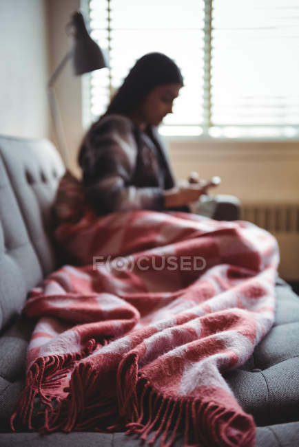 Жінка використовує мобільний телефон, розслабляючись на дивані у вітальні вдома — стокове фото