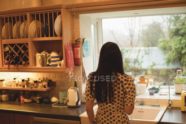 Вид сзади женщины, смотрящей в окно на кухне дома — стоковое фото