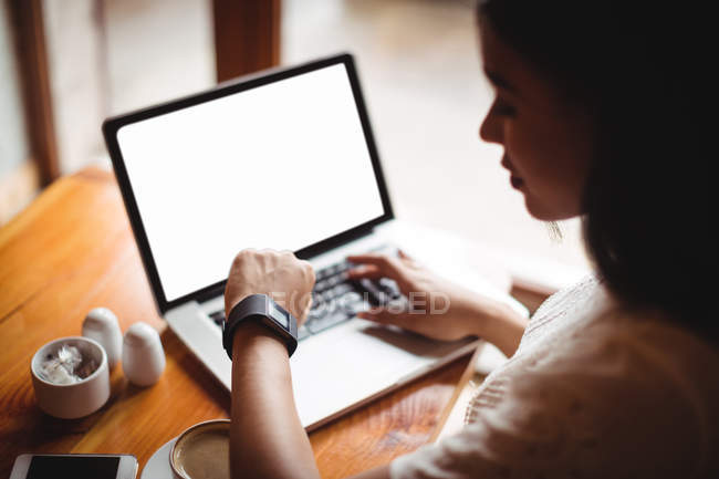 Donna in cerca di tempo durante l'utilizzo di laptop in caffè — Foto stock