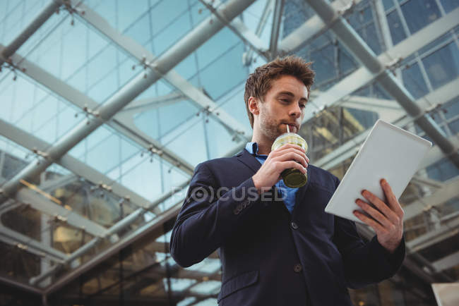 Бізнесмен використовує цифровий планшет, маючи сік біля офісної будівлі — стокове фото