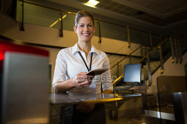 Portrait of female staff holding boarding pass and passport at airport terminal — Stock Photo