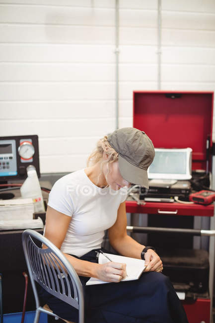 La escritura mecánica femenina en el portátil en el garaje de reparación - foto de stock