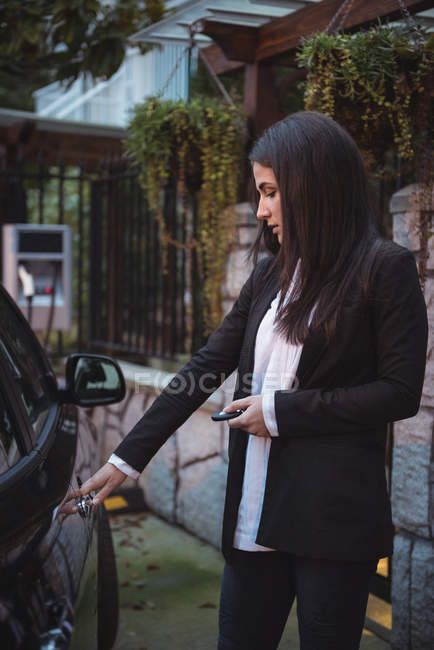 Femme ouvrant la porte de la voiture avec télécommande à la station de recharge du véhicule électrique — Photo de stock