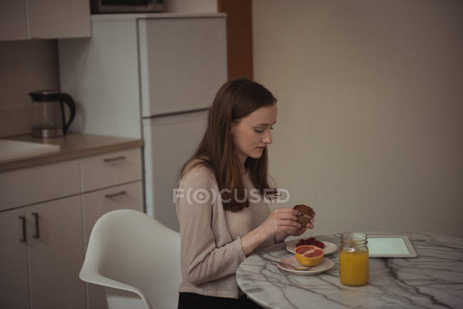 Femme tenant cupcake tout en prenant le petit déjeuner à la maison — Photo de stock