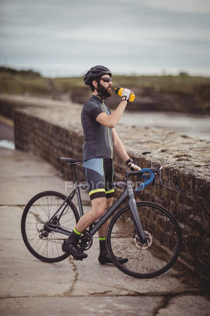 Athlete refreshing from bottle while riding bicycle on road — Stock Photo