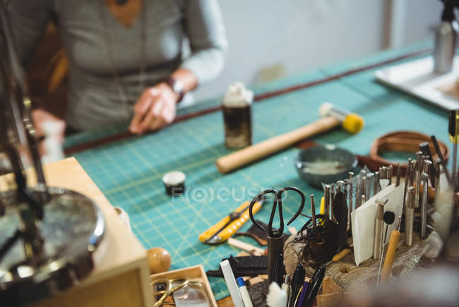 Varias herramientas de trabajo en la mesa en el taller con la mujer trabajando en segundo plano - foto de stock