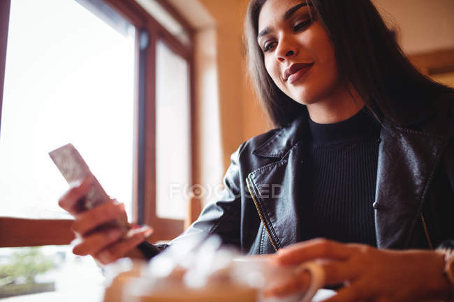 Hermosa mujer usando el teléfono móvil mientras toma una taza de café en la cafetería - foto de stock