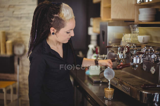 Garçonete derramando leite em xícara de café no balcão no café — Fotografia de Stock