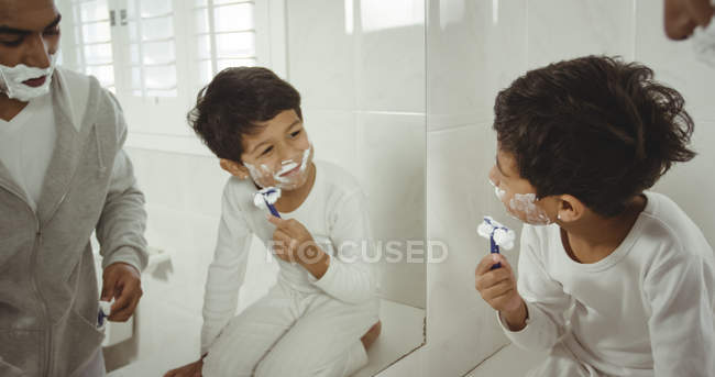 Отец и сын бреются вместе в ванной комнате дома — стоковое фото