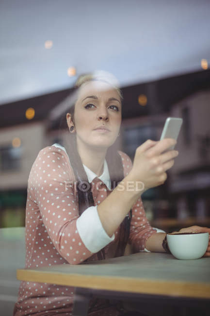 Thoughtful woman using mobile phone while having coffee in cafe — Stock Photo