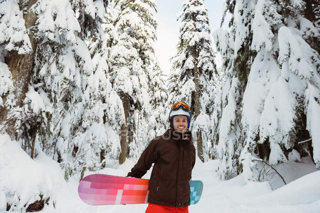 Человек стоит и держит сноуборд на заснеженной горе — стоковое фото