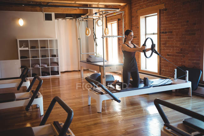 Женщина практикует пилатес на реформаторе с помощью тренажерного кольца в фитнес-студии — стоковое фото