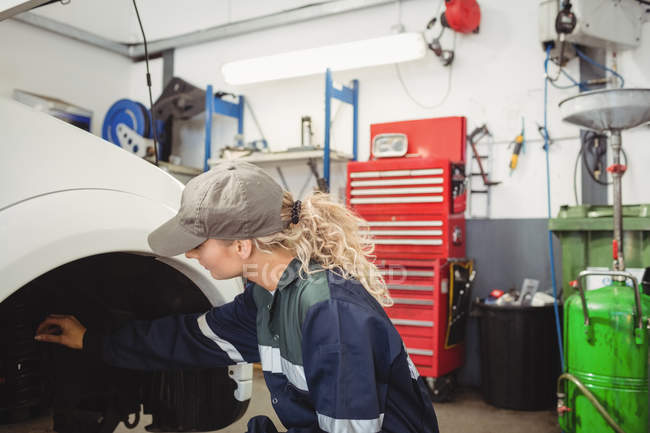 Mecánica femenina examinando un freno de disco de la rueda del coche en garaje de reparación - foto de stock