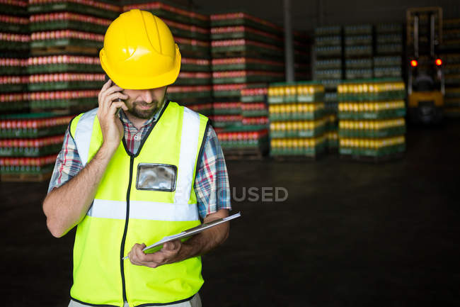 Trabajador masculino sujetando el portapapeles mientras habla por teléfono en la fábrica de jugo - foto de stock