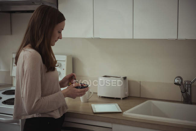 Woman using digital tablet while having breakfast in kitchen at home — Stock Photo