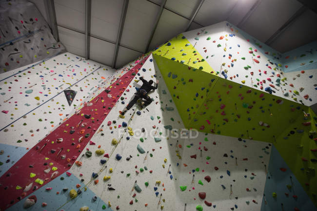 Mann übt Klettern an künstlicher Kletterwand in Turnhalle — Stockfoto