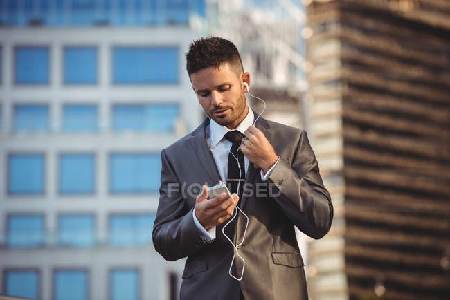Homme d'affaires écoutant de la musique sur un téléphone portable près d'un immeuble de bureaux — Photo de stock