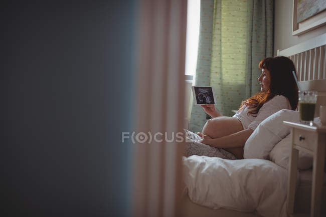 Schwangere betrachtet Sonografie auf digitalem Tisch im Schlafzimmer — Stockfoto