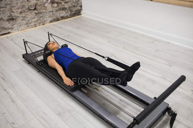 Mujer mintiendo mientras hace ejercicio en reformador en el gimnasio - foto de stock