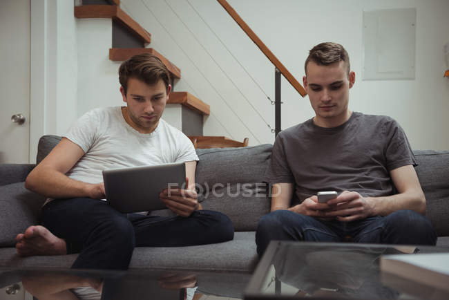 Двое мужчин пользуются цифровым планшетом и мобильным телефоном в гостиной дома — стоковое фото