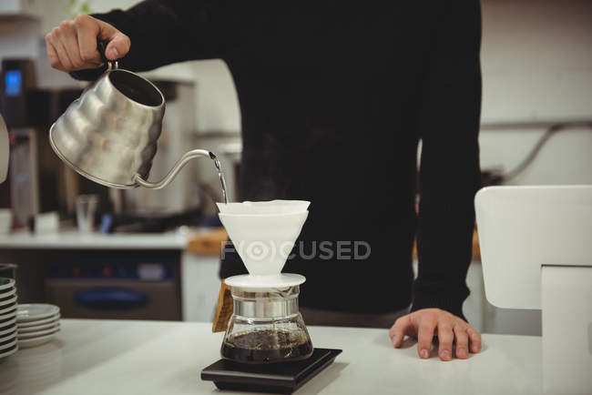 Mid-section of man pouring hot water through funnel in coffee shop — Stock Photo