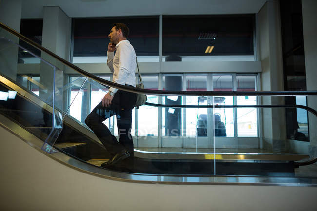 Красивый человек с помощью мобильного телефона на эскалаторе в аэропорту — стоковое фото