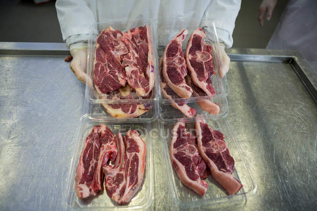 Mid section of butcher holding trays of steaks at meat factory — Stock Photo
